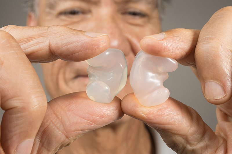 Older man holding up clear earplugs between two fingers Older man holding up clear earplugs between two fingers.